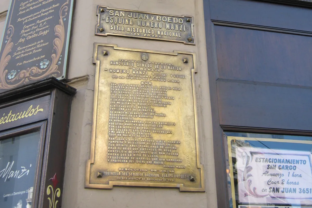 Brass plaques on the corner of Esquina Homero Manzi, one marking the corner as a National Historic Site and a larger one honouring Homero Manzi, beside a painted wooden sign and an iron lamp