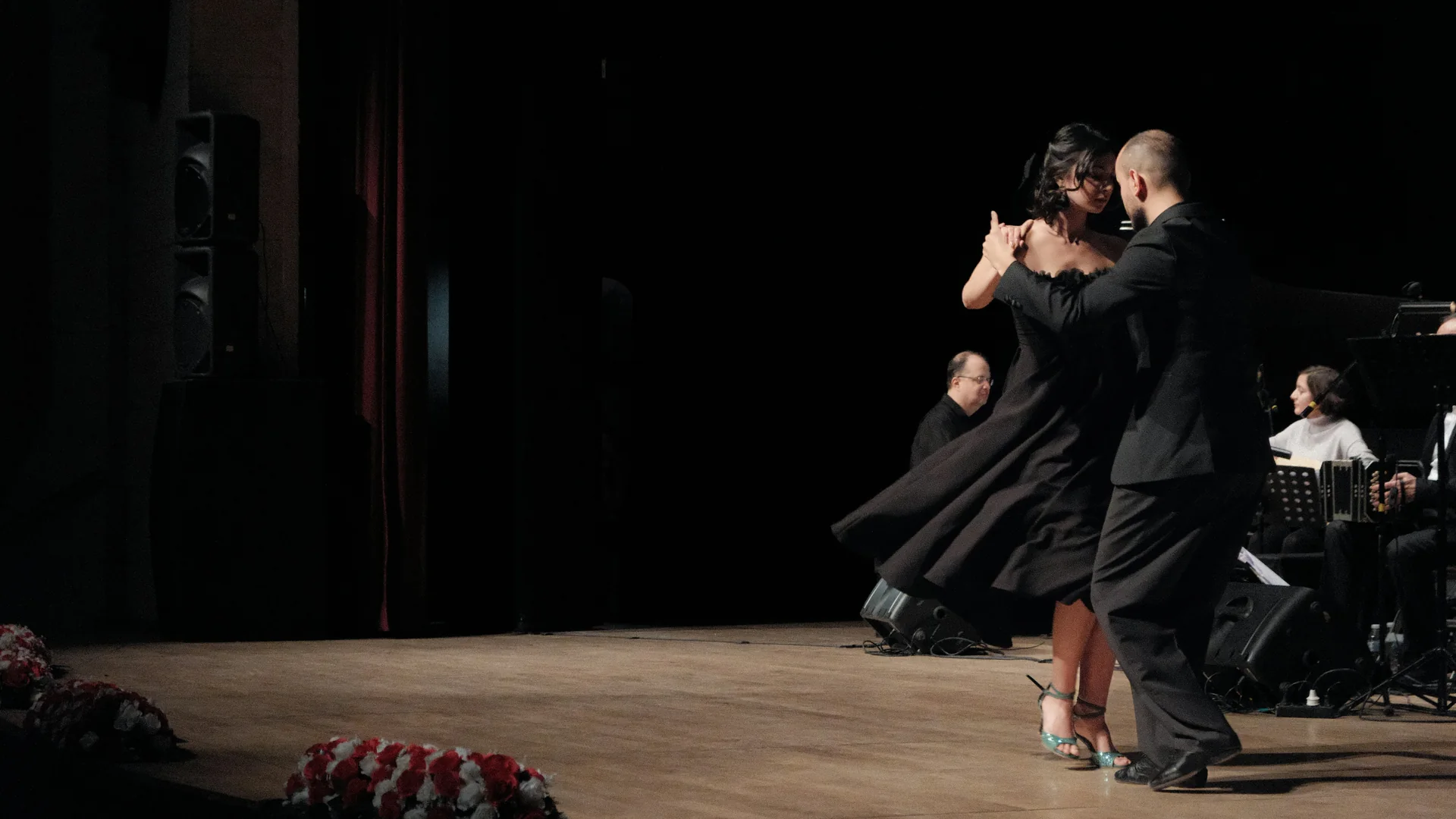 A tango couple in black turning on a wooden stage beside a live ensemble with a bandoneón, photographed in Ankara rather than at Esquina Homero Manzi