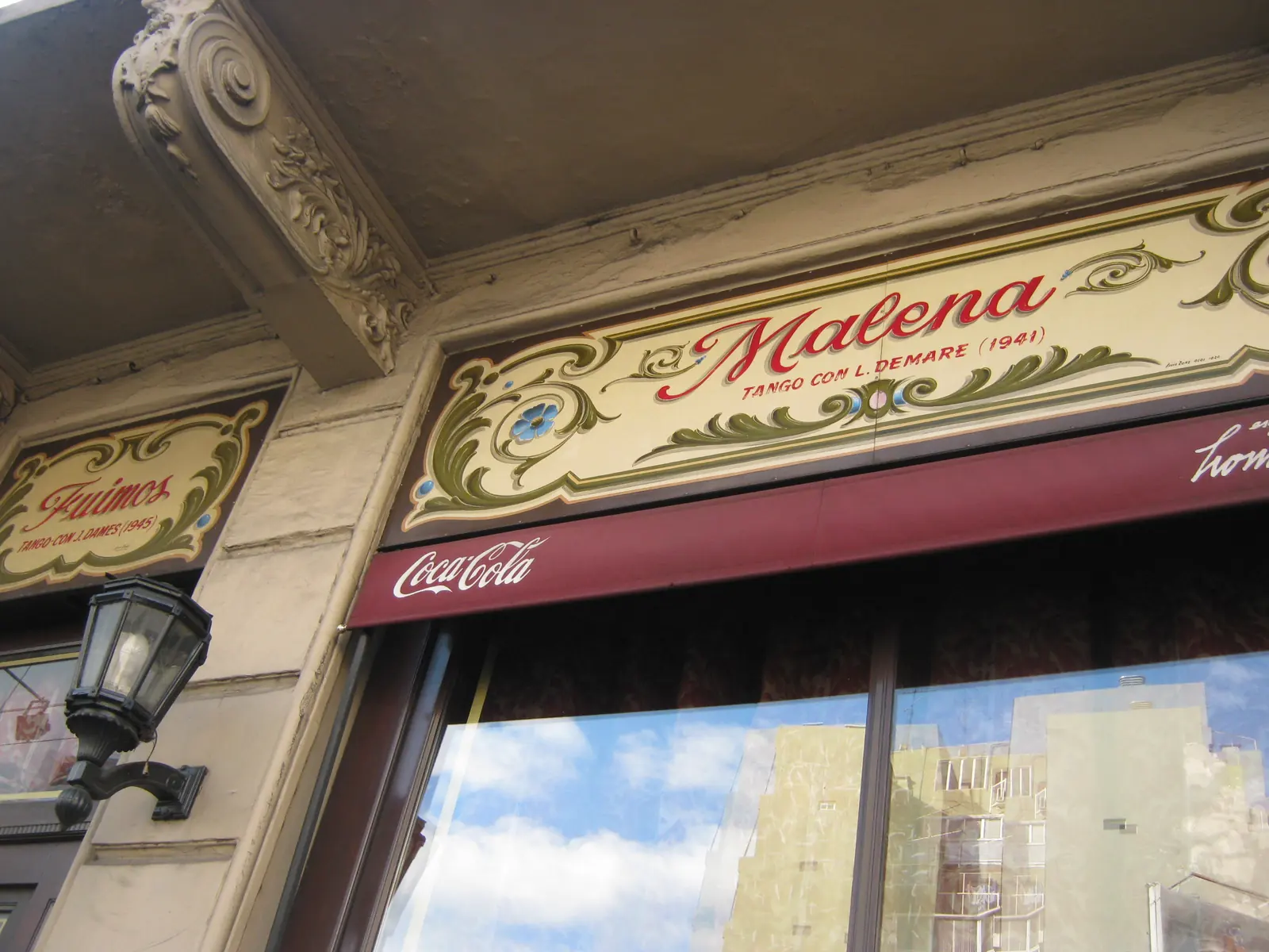 A painted fileteado sign above a window at Esquina Homero Manzi naming the tango Malena, with its composer and year in small letters under the title